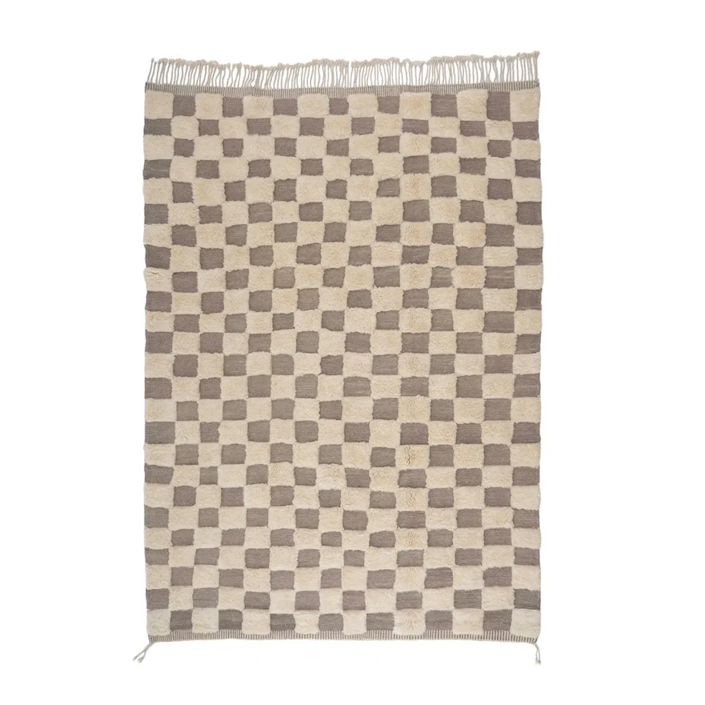 A rectangular beige and brown checkered rug, hand-knotted for a touch of elegance, lies flat on a plain backdrop with fringes adorning one end.