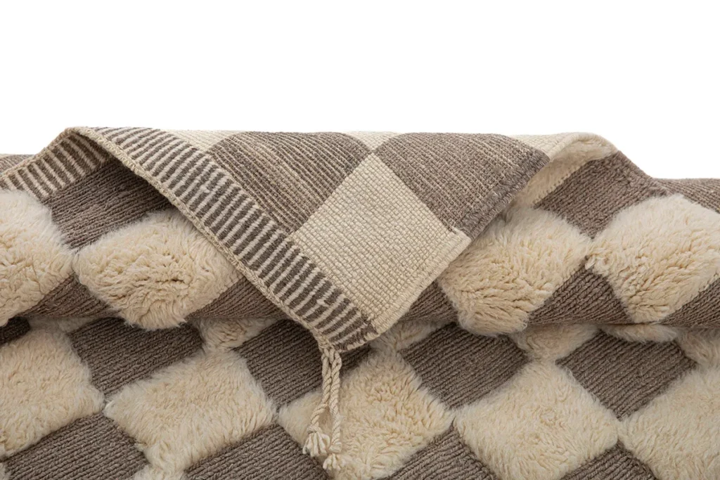 Experience the elegance of a hand-knotted, beige and brown checkered rug with a tassel, set against a crisp white background. This luxury rug epitomizes sophistication and style for any living space.