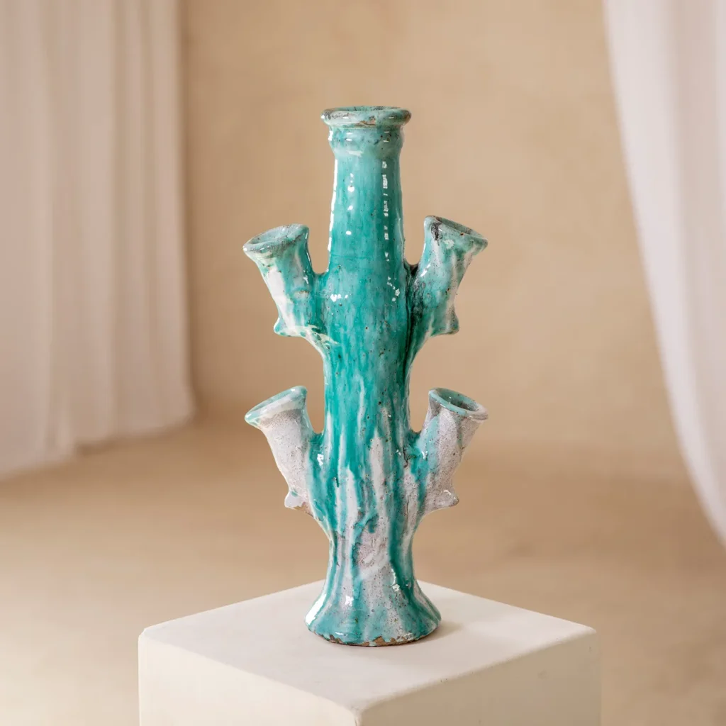 A turquoise cactus-shaped ceramic vase with multiple branches, placed on a white pedestal against a neutral background.