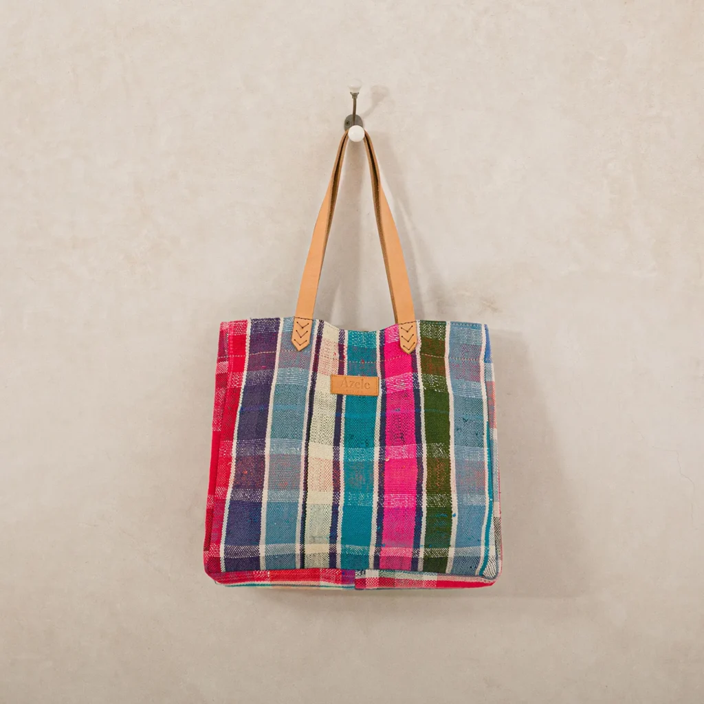 Colorful plaid tote bag with tan leather handles hangs on a wall hook.