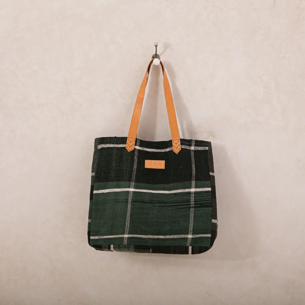 A green plaid tote bag with tan leather handles hangs on a wall hook.