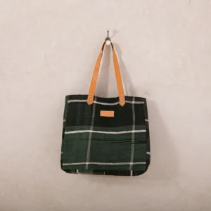 A green plaid tote bag with tan leather handles hangs on a wall hook.
