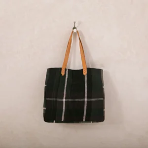 A black-and-white plaid tote bag with tan leather handles hangs on a wall hook.