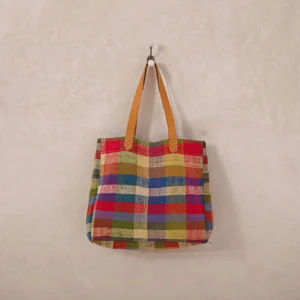 A colorful plaid tote bag with brown handles hangs on a wall hook.