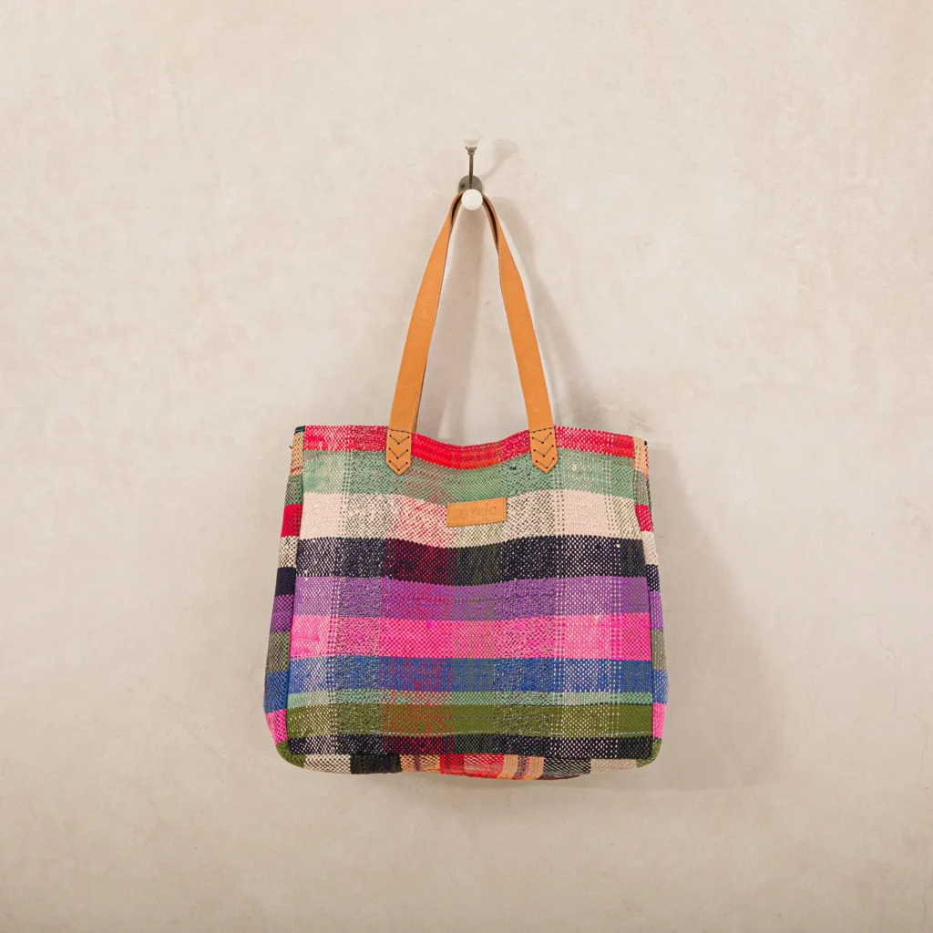 A colorful woven tote bag with leather handles hangs on a wall hook.