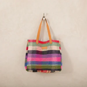 A colorful woven tote bag with leather handles hangs on a wall hook.
