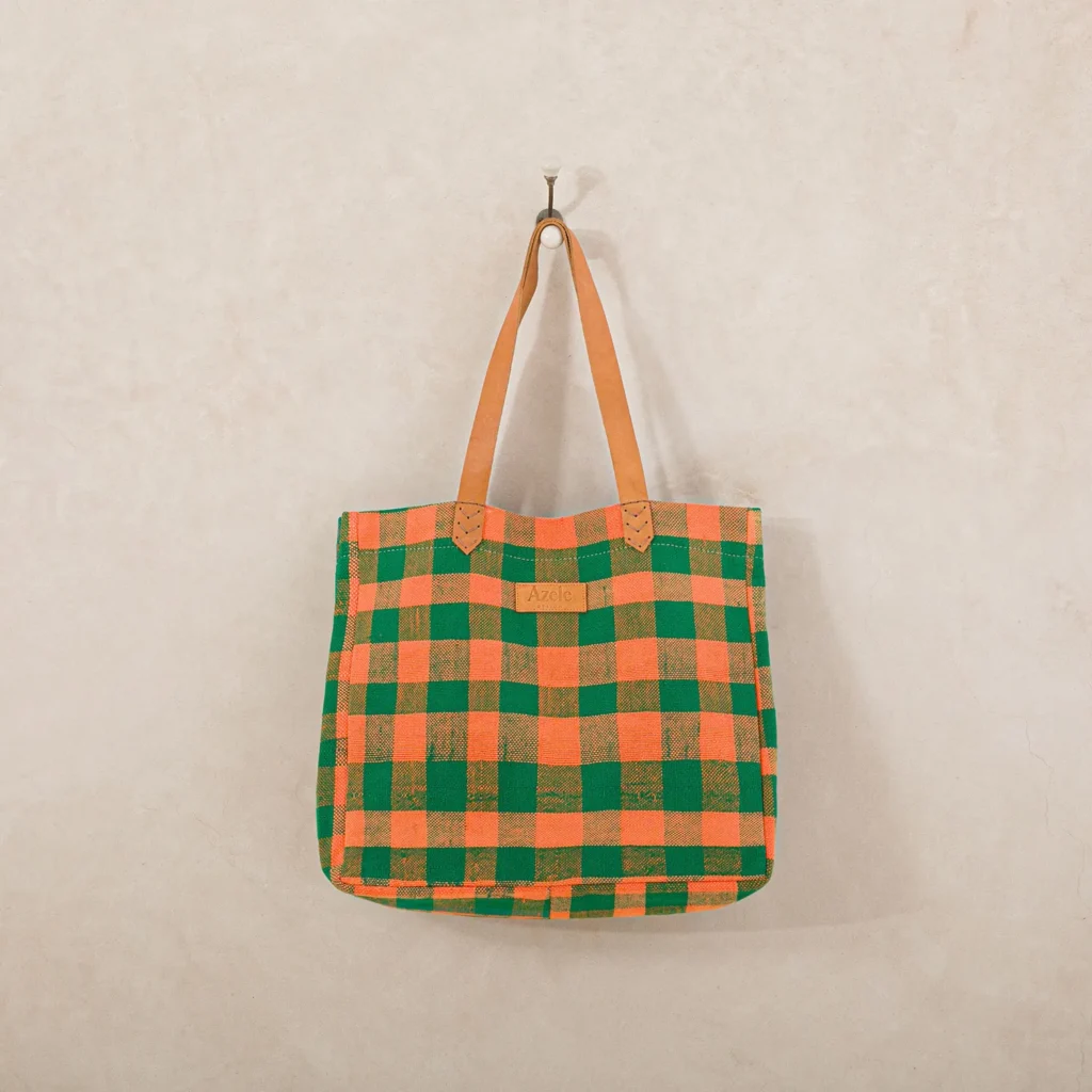 A checkered tote bag with green and orange squares hangs on a wall hook.