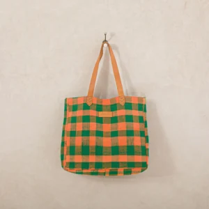 A checkered tote bag with green and orange squares hangs on a wall hook.