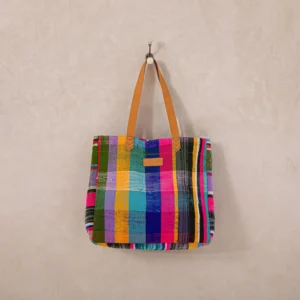 Multicolored plaid tote bag with tan leather handles hanging on a wall hook.
