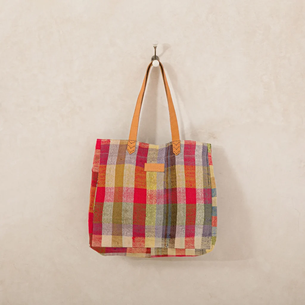 A vibrant plaid tote bag with leather straps hangs elegantly on a wall hook, perfectly blending functionality and style.