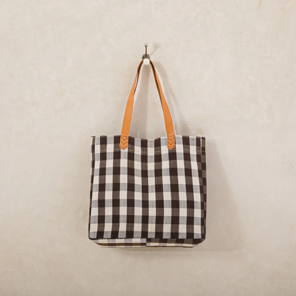 A black and white checkered tote bag with orange handles hangs on a wall-mounted hook.