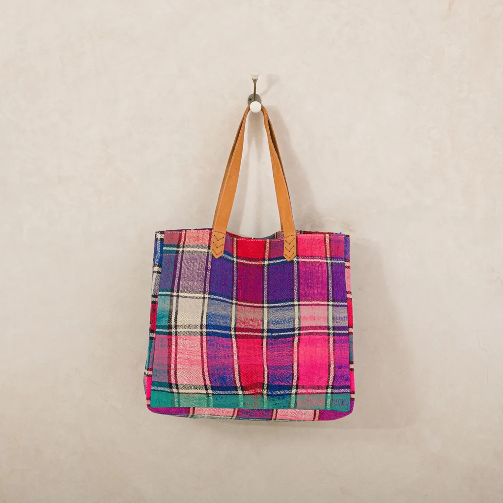 Colorful plaid tote bag with leather handles hanging on a hook against a plain wall.
