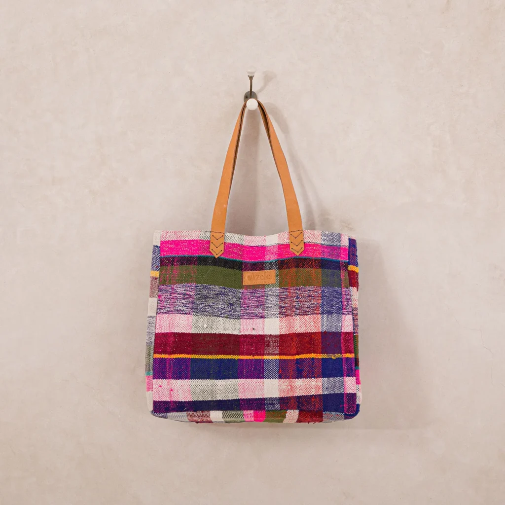 Multicolored plaid tote bag with brown leather handles hanging on a wall hook.