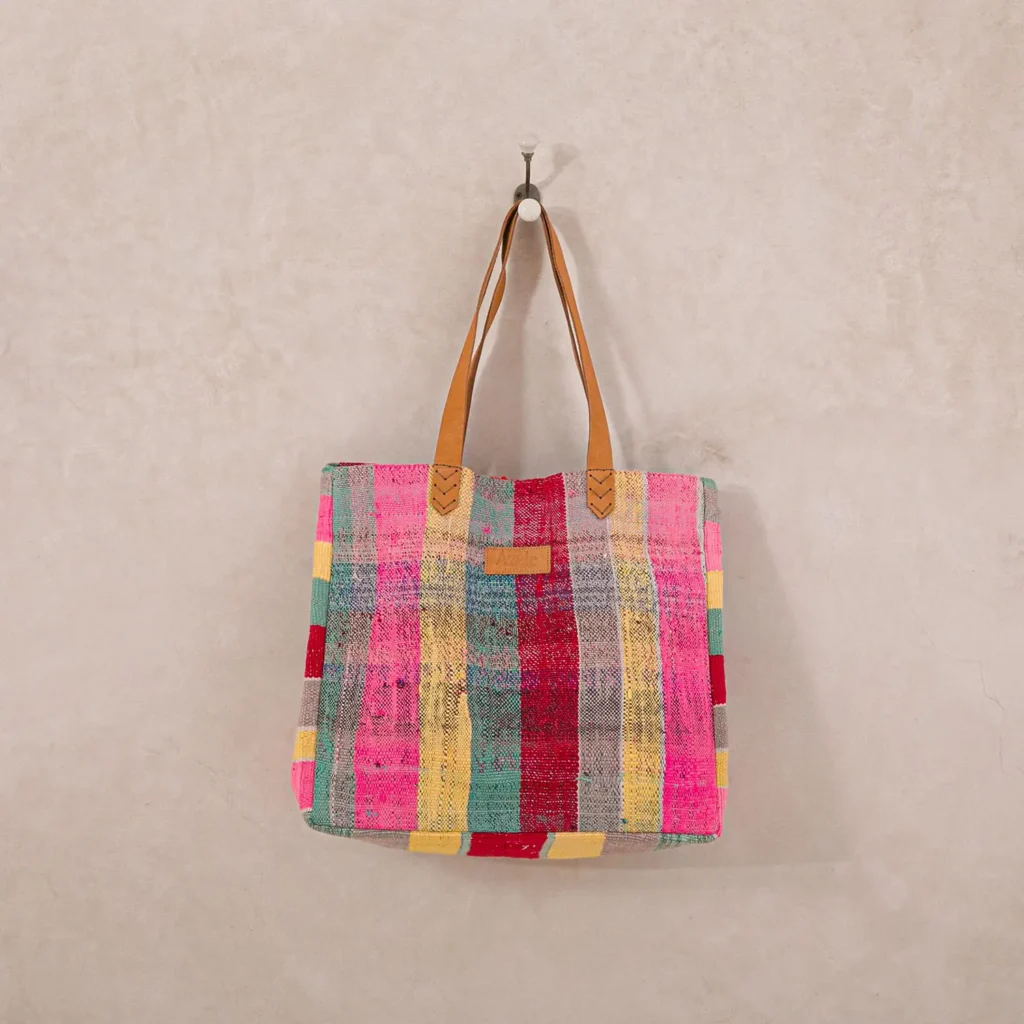 A colorful, striped tote bag with brown handles hangs on a wall hook.