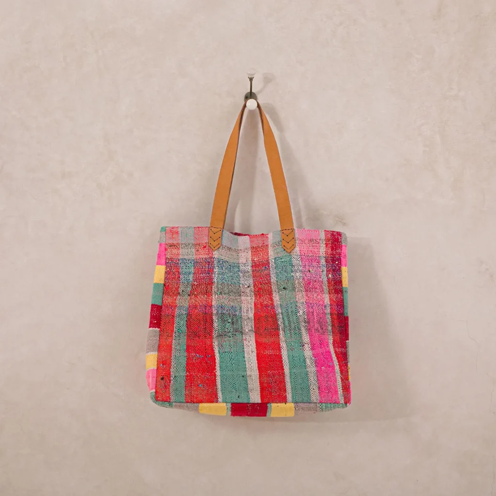 Colorful patchwork tote bag with leather straps hanging on a wall hook.