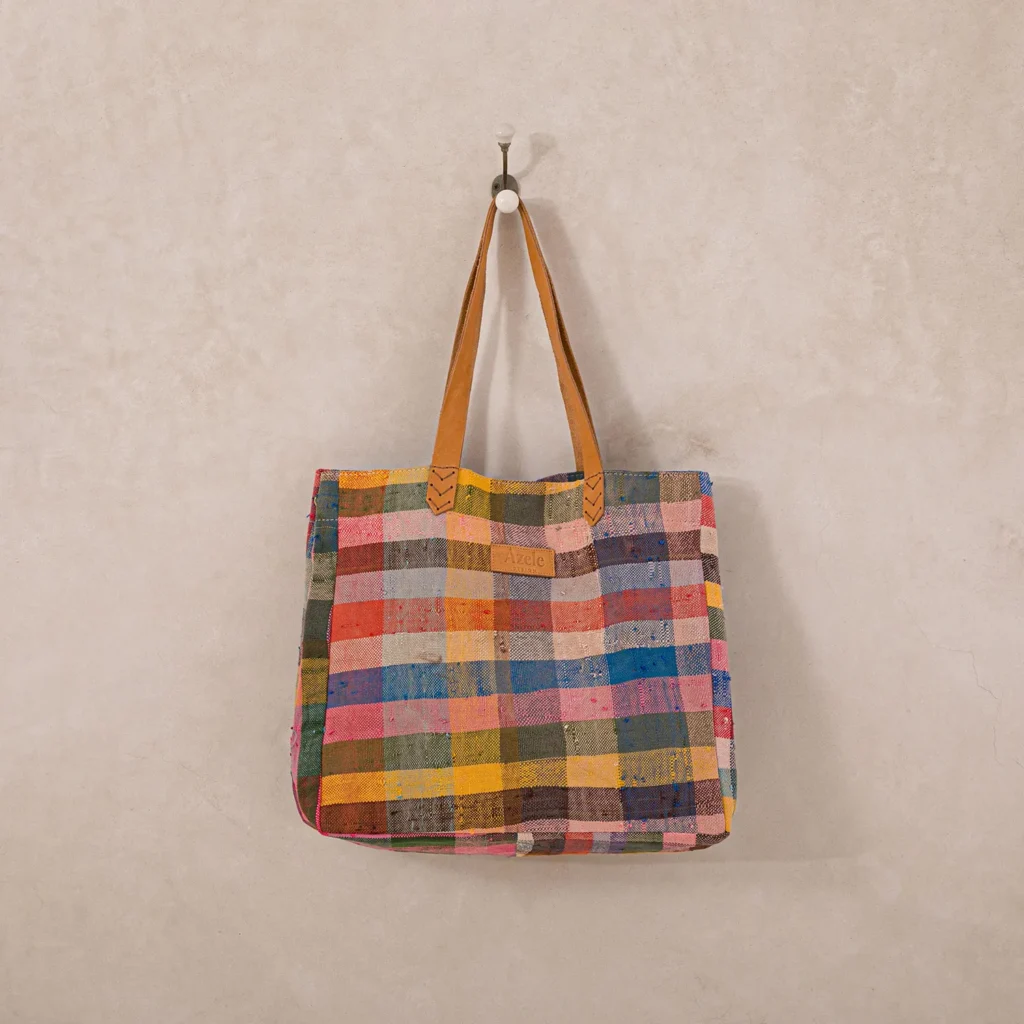 Patchwork tote bag with colorful squares hangs on a wall hook.