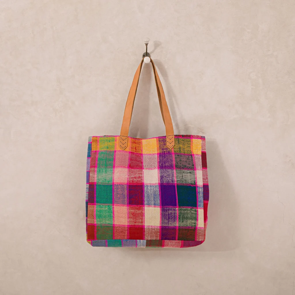 A colorful, plaid-patterned tote bag with leather straps hangs on a wall hook.