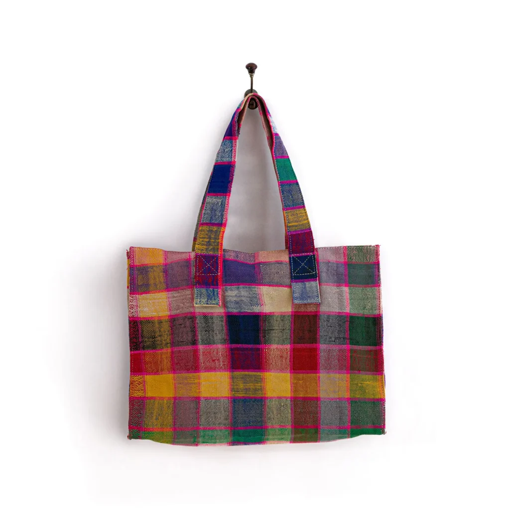 A multicolored plaid fabric tote bag hangs on a wall hook.