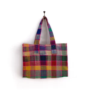 A multicolored plaid fabric tote bag hangs on a wall hook.