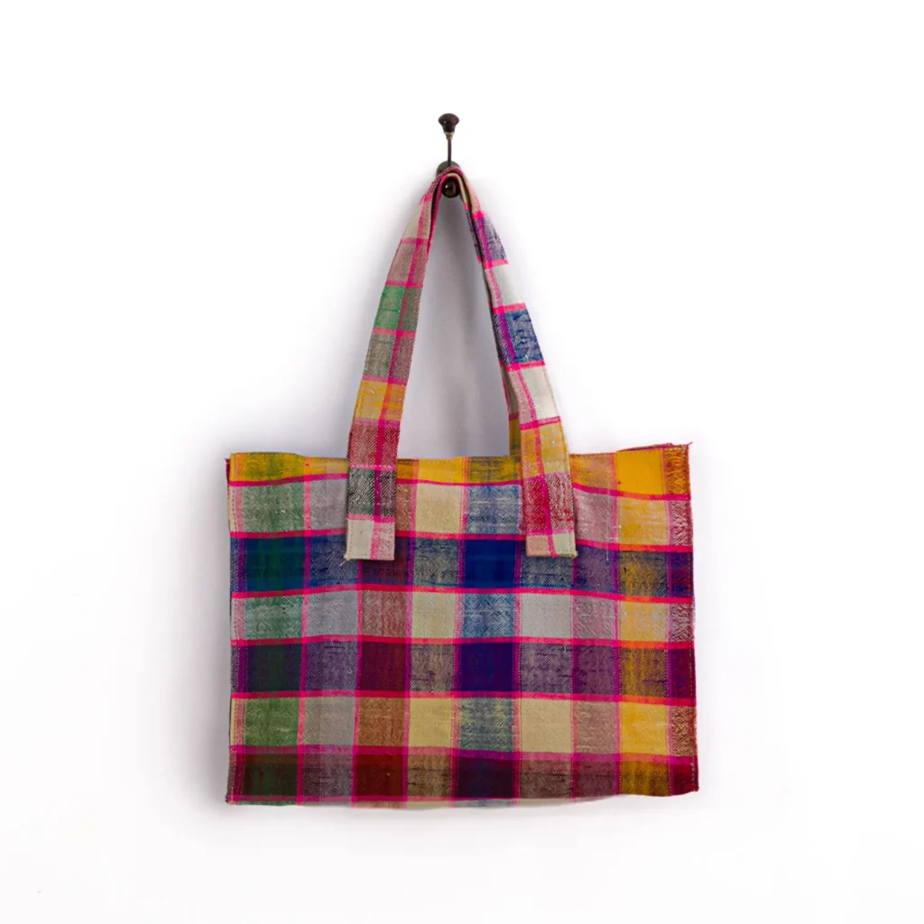 Multicolored checkered tote bag with two handles hanging on a wall hook.