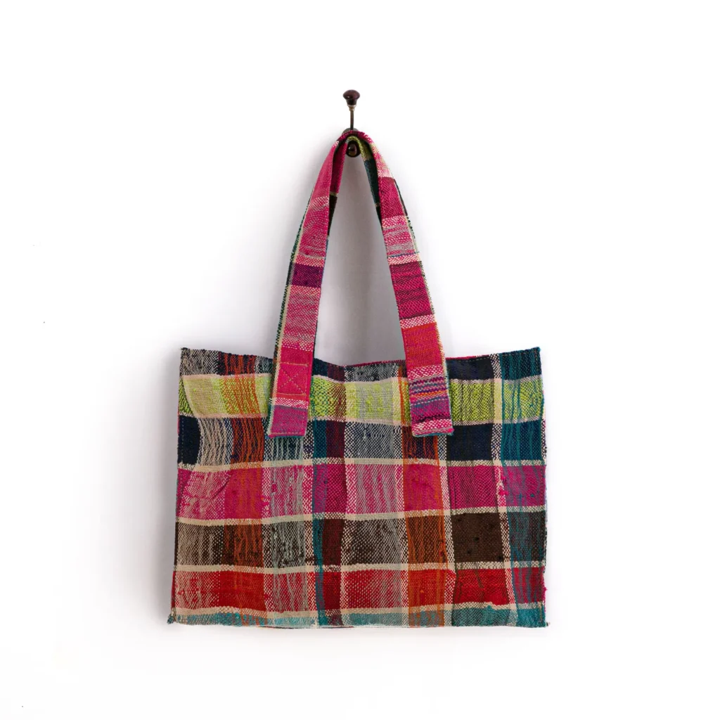 A multicolored patchwork tote bag with a checkered pattern hangs on a wall hook.