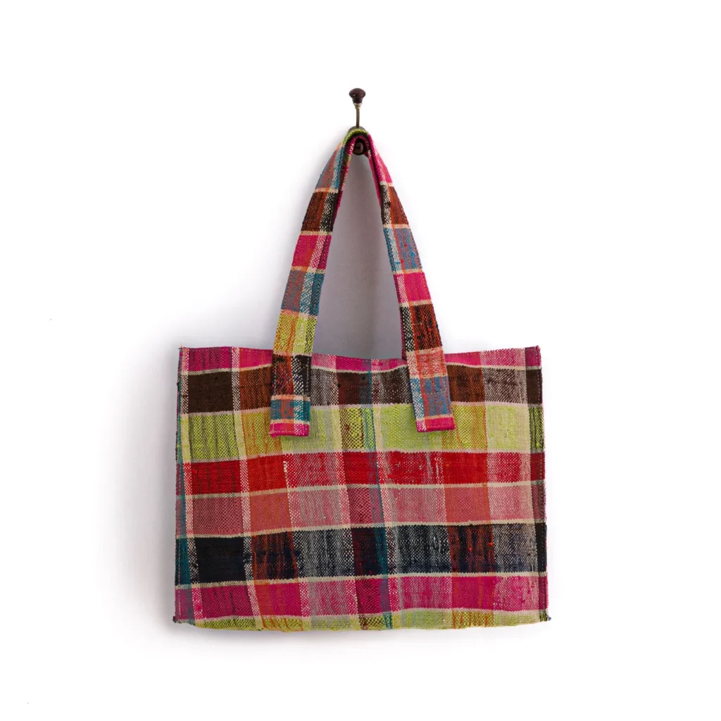 Multicolored plaid tote bag with two handles, hanging on a wall hook.