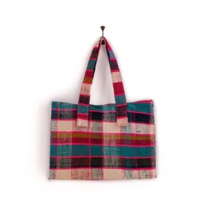 A multicolored plaid fabric tote bag hangs on a wall hook.