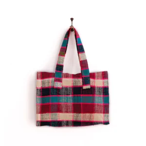 A plaid-patterned tote bag with red, blue, and beige colors hangs on a peg against a white background.