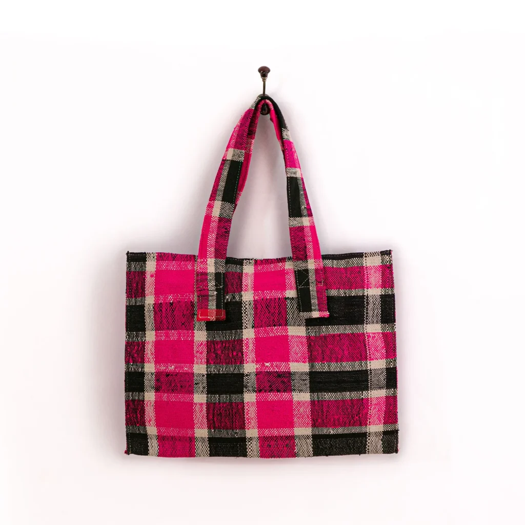 Pink and black plaid tote bag with two handles, hanging on a hook against a plain white background.