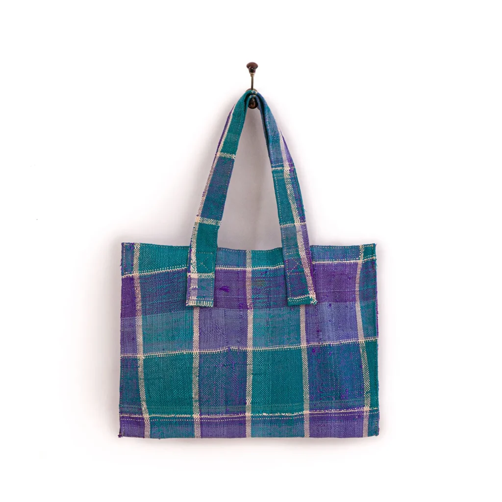 A blue and purple plaid tote bag with two straps hanging on a single nail against a plain white background.