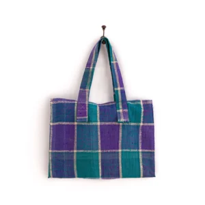 An upcycled weekend bag boasts a plaid design with purple and teal checkered patterns, elegantly hanging on a wall hook.