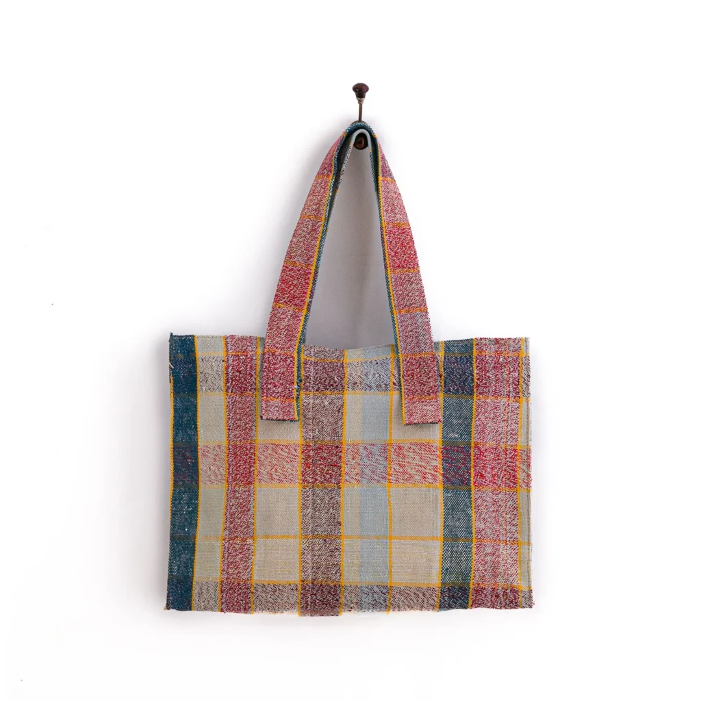 A multicolored, checkered tote bag with two handles hangs on a wall hook.