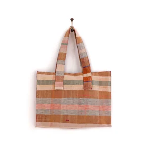 A woven tote bag with horizontal stripes in beige, pink, and orange hues hangs from a wall hook.