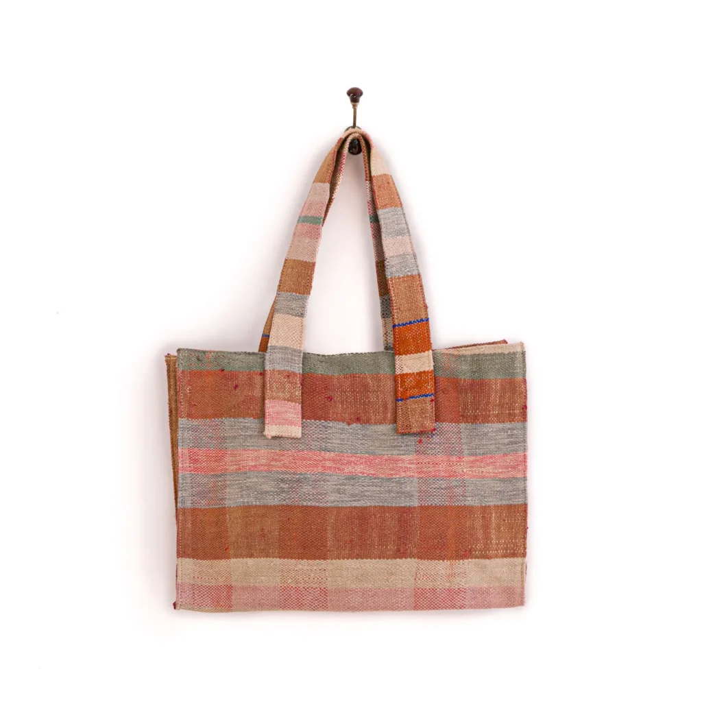 A woven tote bag with a checkered pattern in shades of pink, brown, and beige hangs from a wall hook.