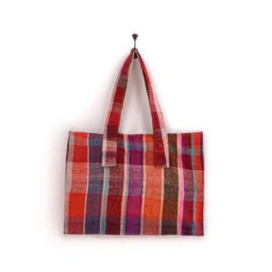 Handmade patchwork bag with a colorful checkered pattern, featuring red, pink, orange, and brown squares, hung on a wall hook.