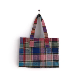 A multicolored patchwork tote bag with striped patterns hangs on a single hook against a white wall.