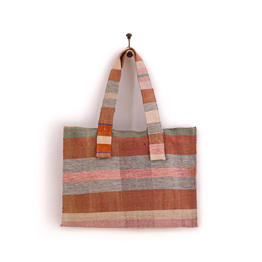 Woven tote bag with multicolored stripes, hanging on a single hook.