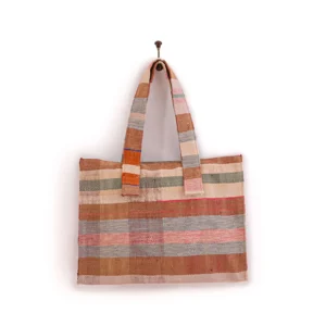 A rectangular woven tote bag with horizontal stripes in shades of brown, gray, and pink hangs from a hook. It has two sturdy handles.