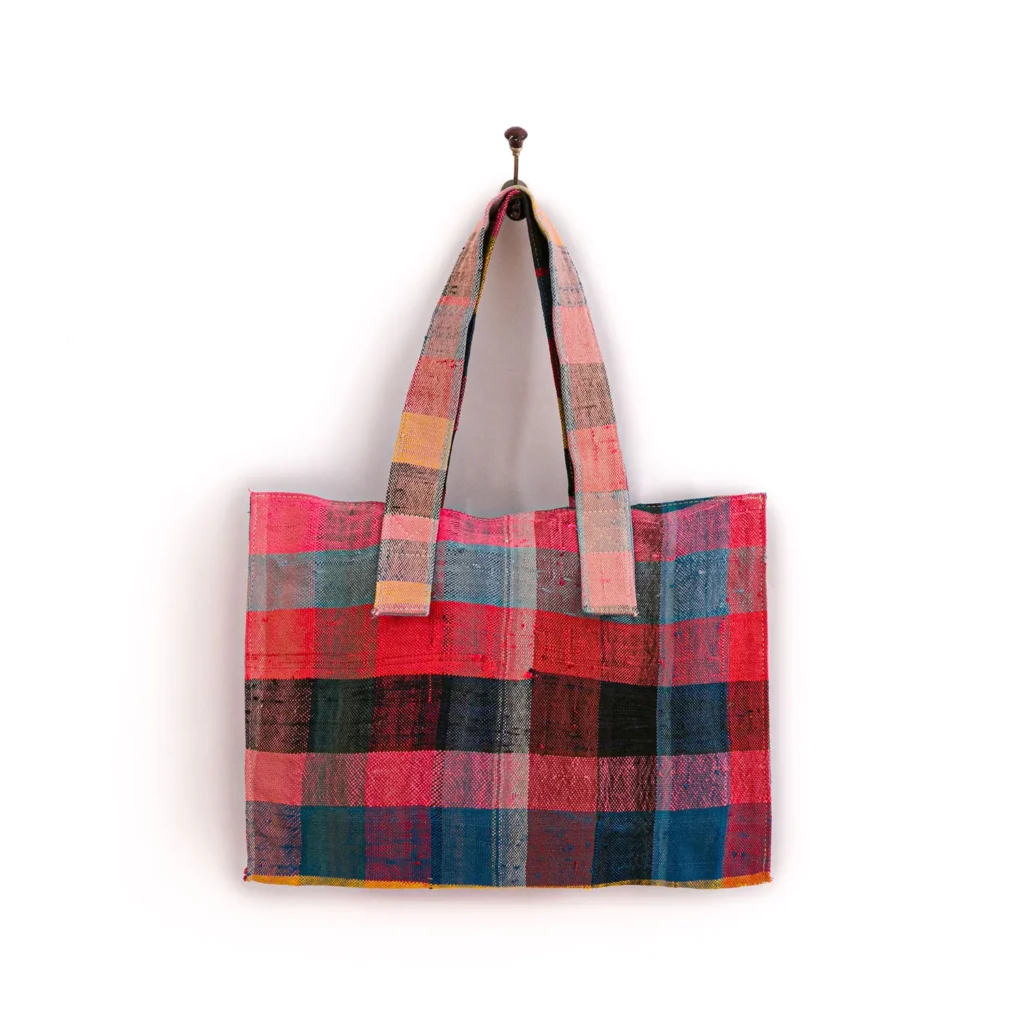 A multicolored patchwork tote bag with a checkered pattern hangs on a single nail against a plain background.