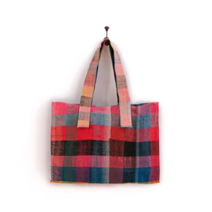 A multicolored patchwork tote bag with a checkered pattern hangs on a single nail against a plain background.