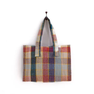 A multicolored patchwork tote bag with a checkered pattern hangs on a wall hook.