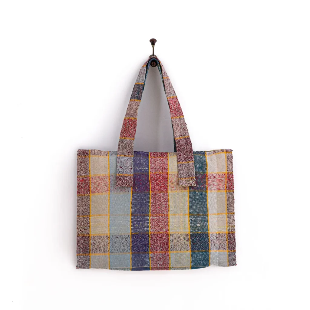 Multicolored patchwork tote bag with two handles, hanging on a hook against a white background.