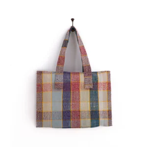 Multicolored patchwork tote bag with two handles, hanging on a hook against a white background.