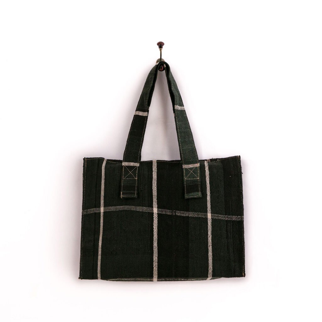 A black and gray plaid tote bag hanging on a single hook against a plain white background.