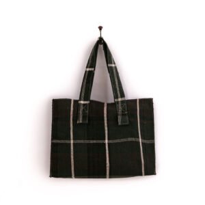 A black and white plaid tote bag hangs on a wall hook against a plain white background.