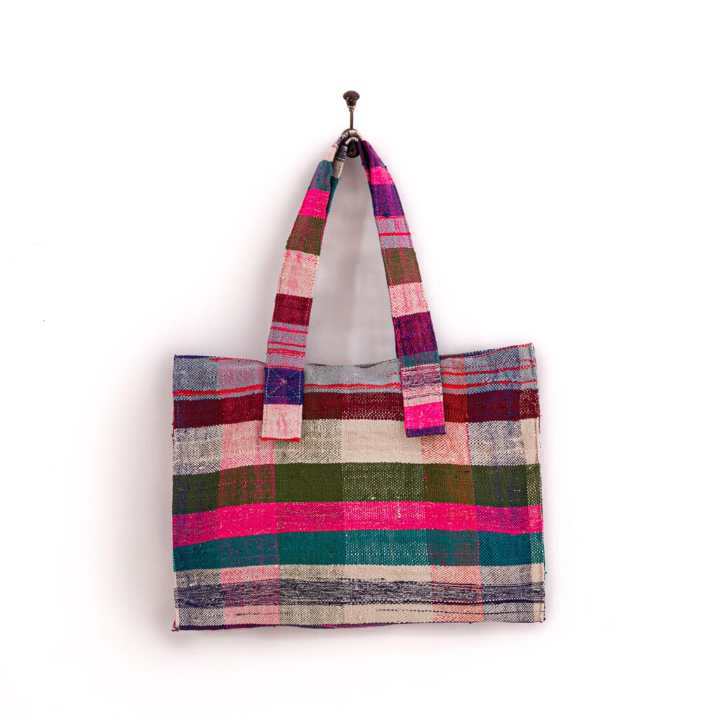 A multicolored plaid tote bag with wide handles is hanging on a hook against a white background.