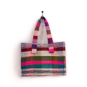 A multicolored plaid tote bag with wide handles is hanging on a hook against a white background.