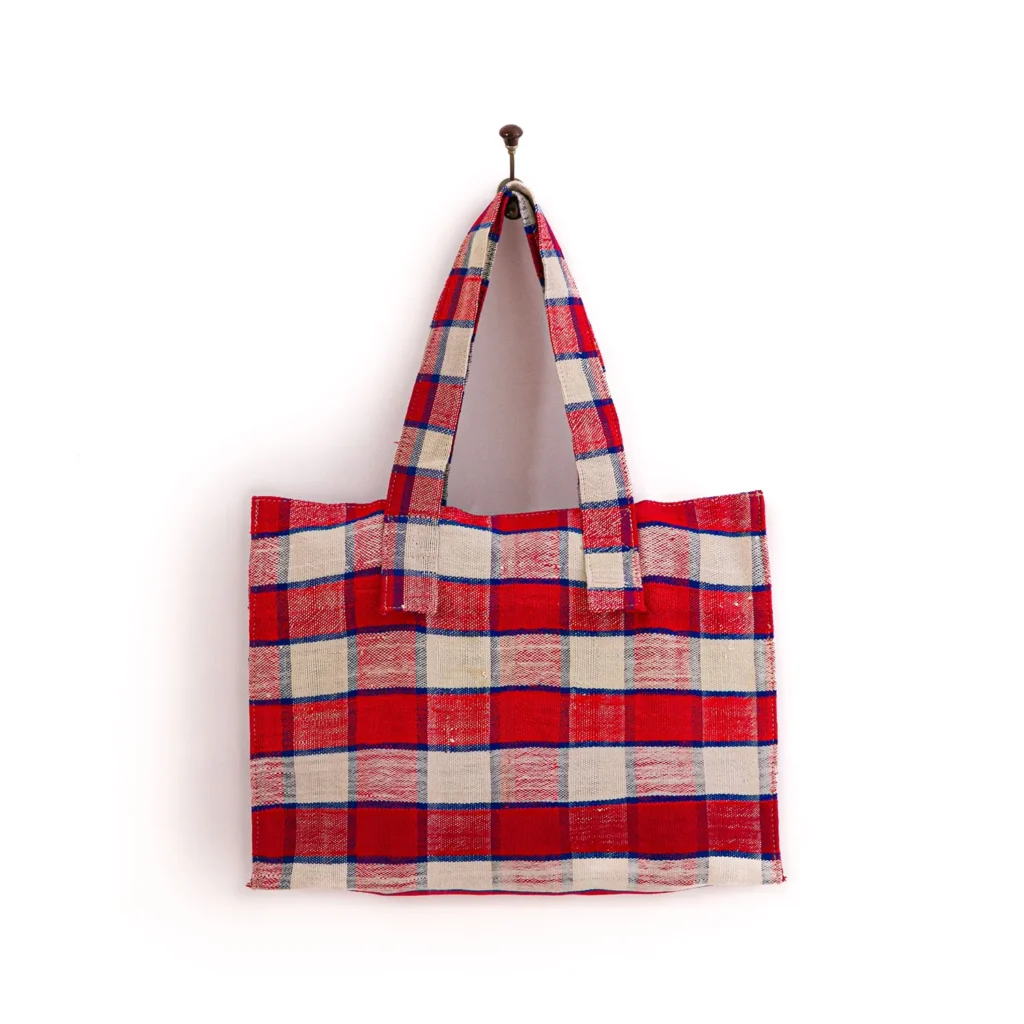 Red, white, and blue checkered fabric tote bag with two handles, hanging on a hook against a plain white background.