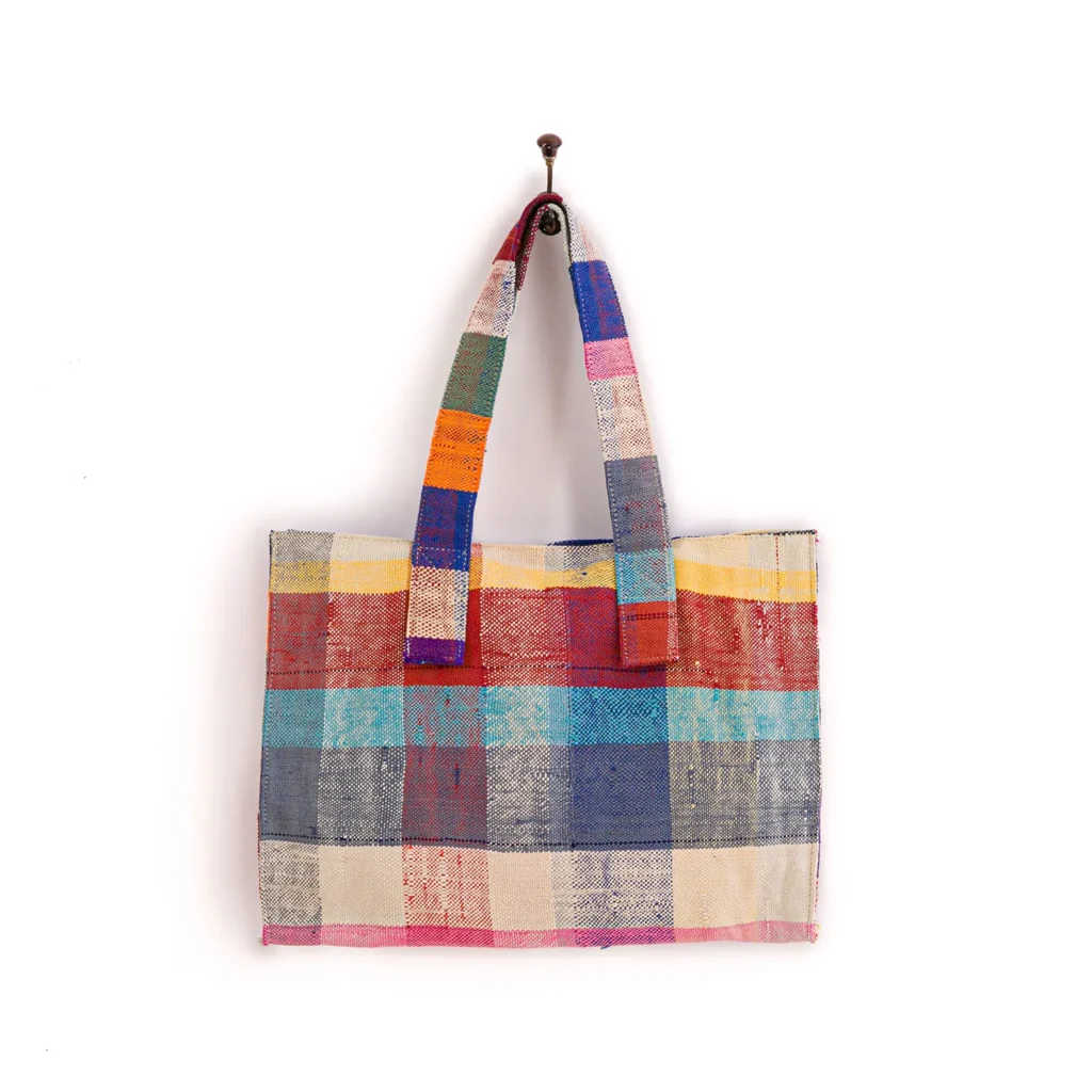 A multicolored, plaid-patterned tote bag hangs on a wall hook.