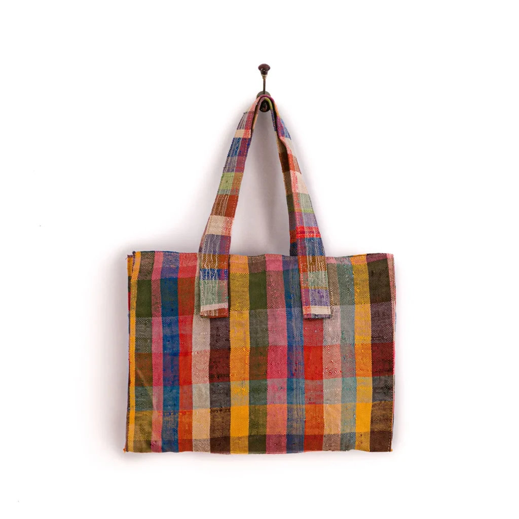 Multicolored plaid fabric tote bag hanging on a wall hook.